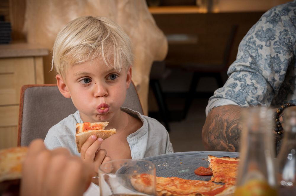 Blond boy eating a slice of pizza at a table.