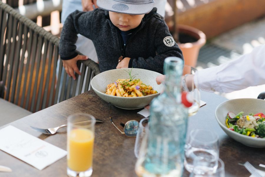 Bambino che guarda un piatto di pasta in un ristorante con un bicchiere di succo d'arancia sul tavolo.