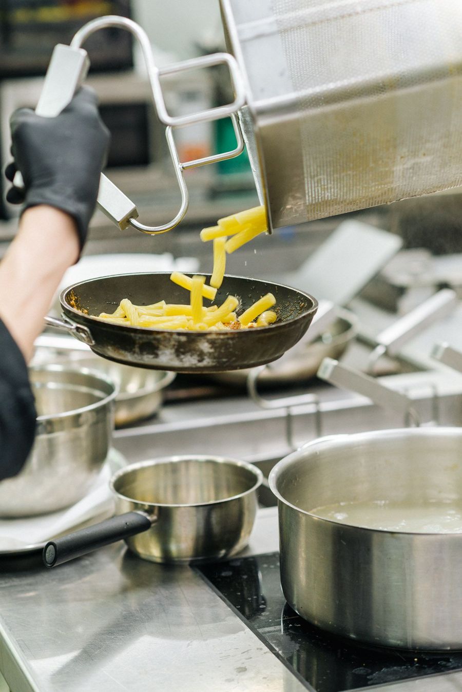 Pasta scolata da una pentola e versata in una padella in cucina.