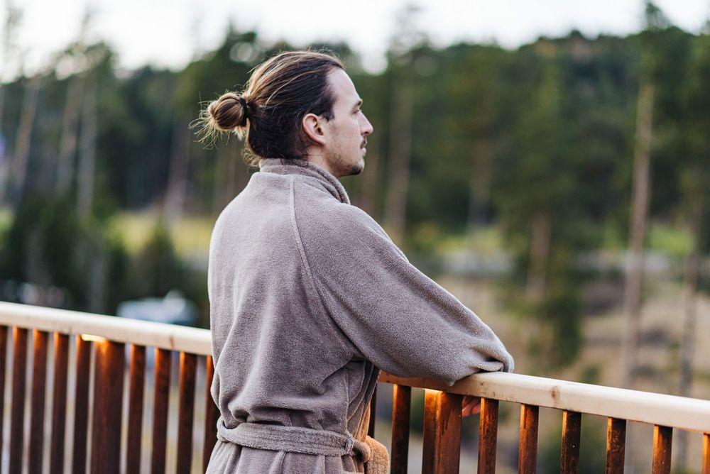 Uomo con accappatoio marrone guarda il paesaggio da un balcone di legno Uomo con accappatoio marrone guarda il paesaggio da un balcone di legno