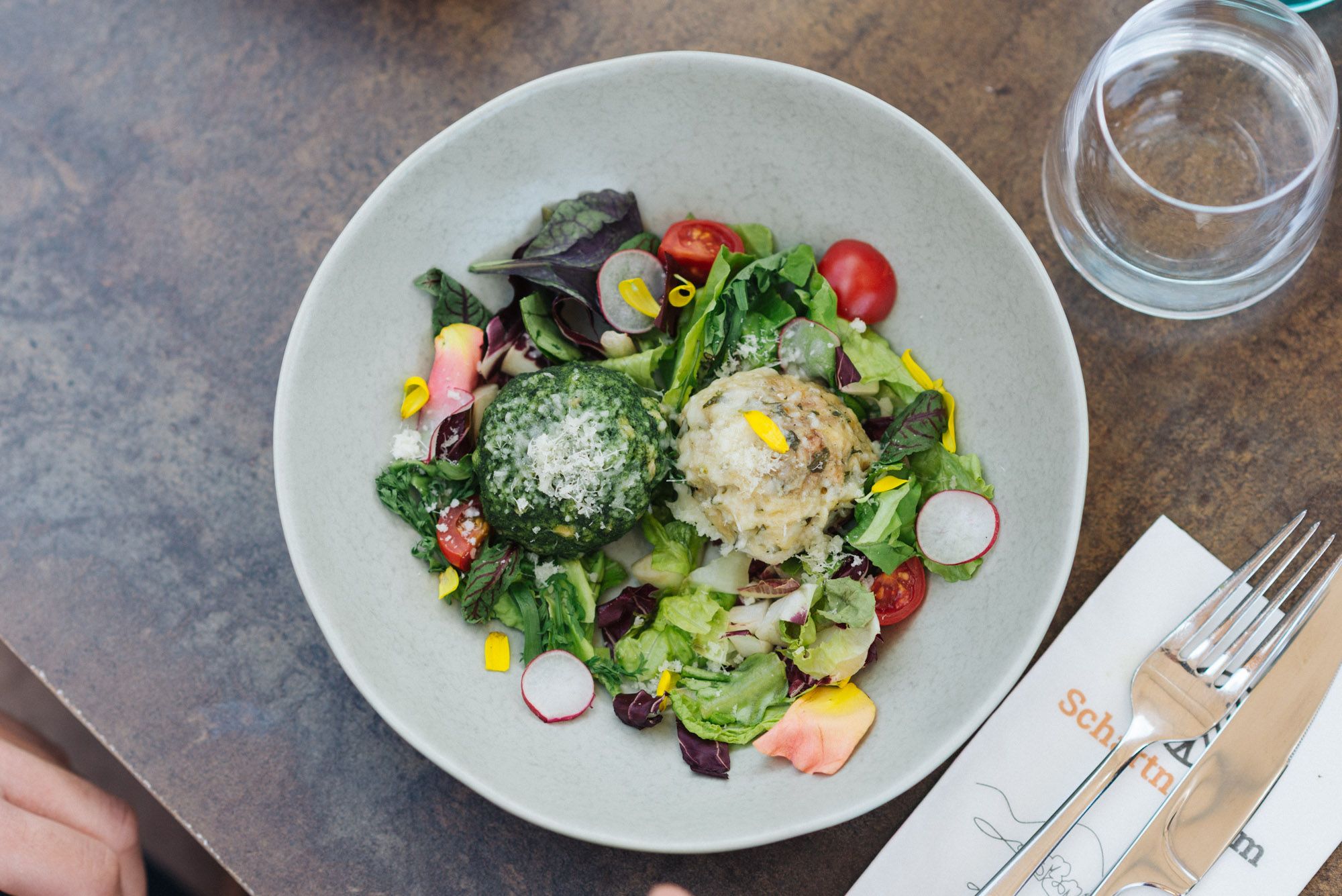 Salat mit zwei Klößen und geriebenem Käse in weißem Teller, daneben Glas und Besteck